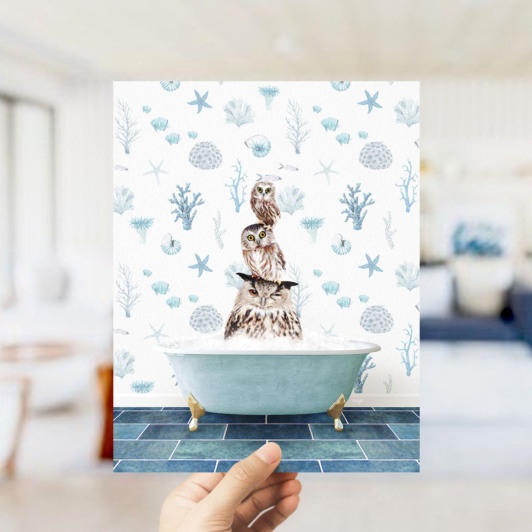 A hand is holding up a framed image of three owls sitting in a bathtub, surrounded by a pattern of seashells, starfish, and other marine life.