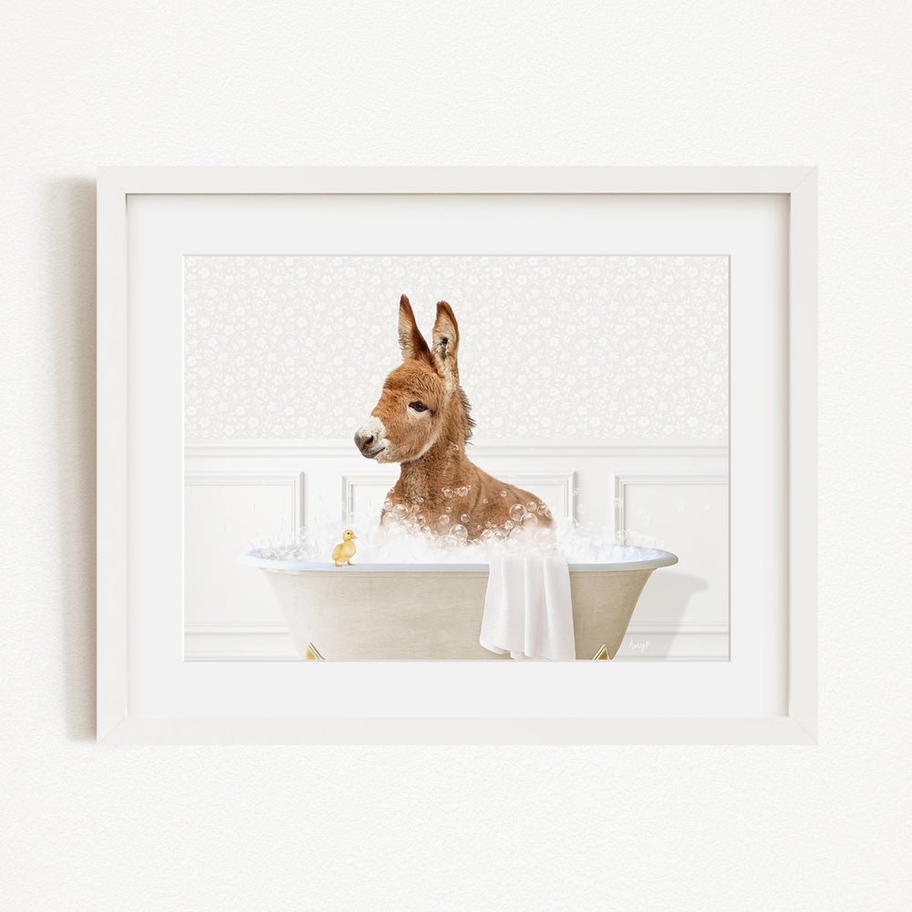 A brown donkey is sitting in a white bathtub filled with bubbles, with a yellow duck nearby.