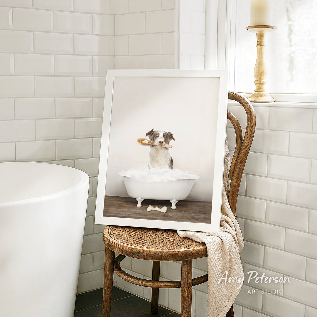 A framed photograph of a dog sitting in a bathtub, holding a toy, is displayed on a wooden chair in a bathroom setting.