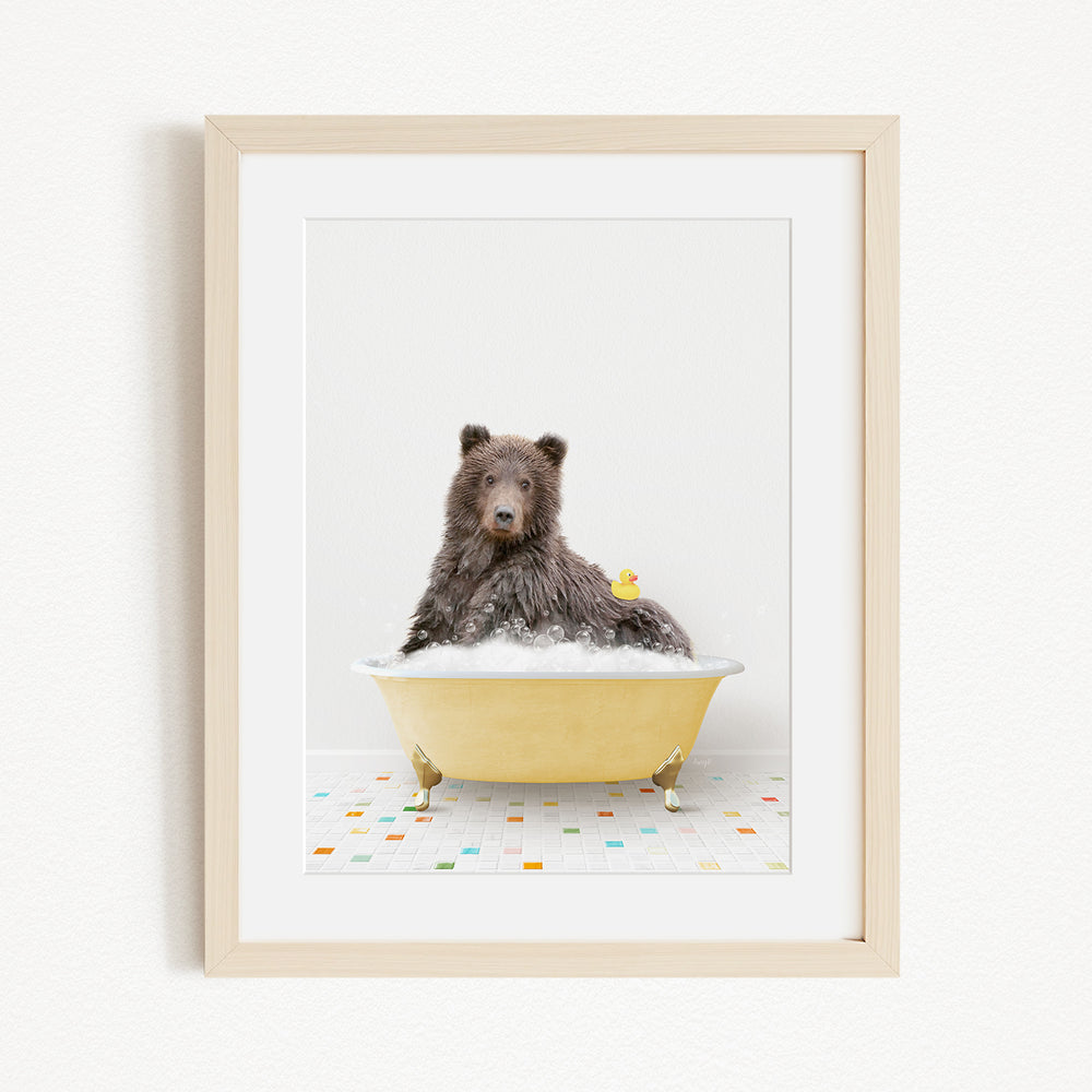 A brown bear sitting in a yellow bathtub filled with bubbles, with a yellow rubber duck floating on the water.