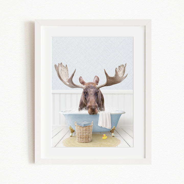 A moose with large antlers is sitting in a bathtub filled with water, surrounded by a basket of rubber ducks and a yellow rubber ducky.