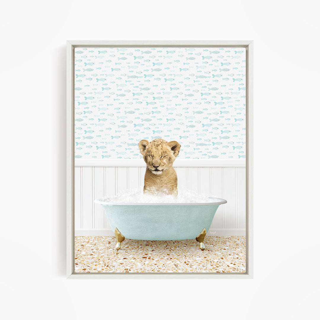 A young lion cub sitting in a blue bathtub filled with water, surrounded by a pattern of fish.