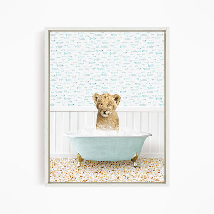 A young lion cub sitting in a blue bathtub filled with water, surrounded by a pattern of fish.