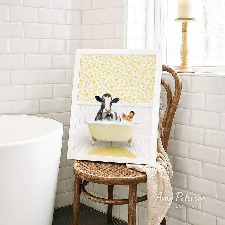 A framed image of a cow and a chicken sitting in a bathtub, with a yellow floral pattern on the wall behind them.