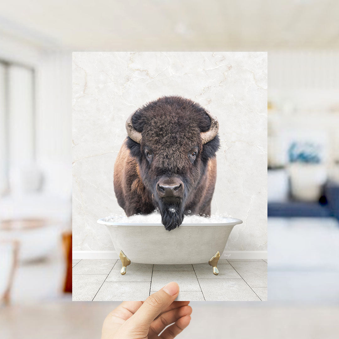 A hand holds up a framed image of a bison in a bathtub, creating a whimsical and humorous scene.