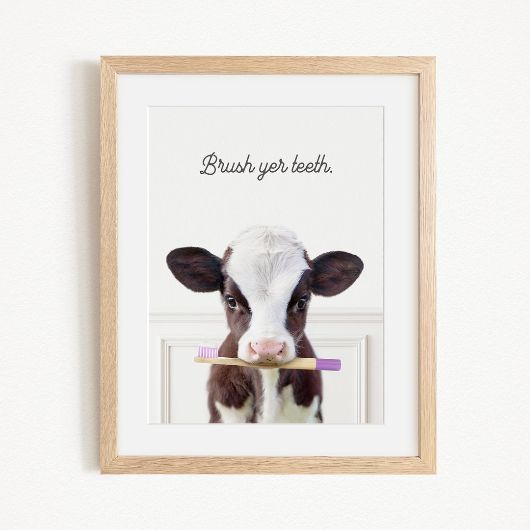 A framed image of a cow holding a toothbrush in its mouth, with the text "Brush yer teeth."