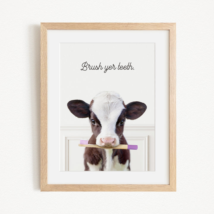 A framed image of a cow holding a toothbrush in its mouth, with the text "Brush yer teeth."