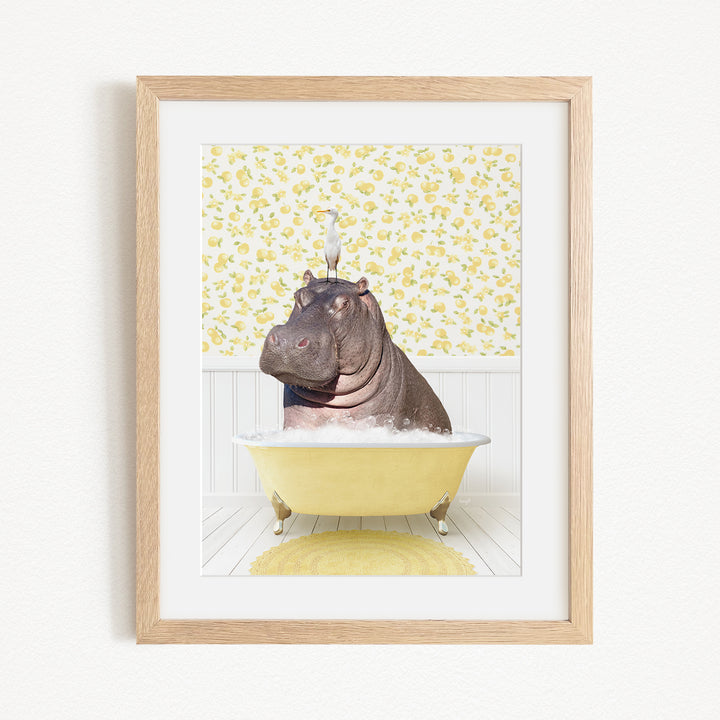 A framed image depicting a hippopotamus sitting in a yellow bathtub filled with water, with a bird perched on its head.