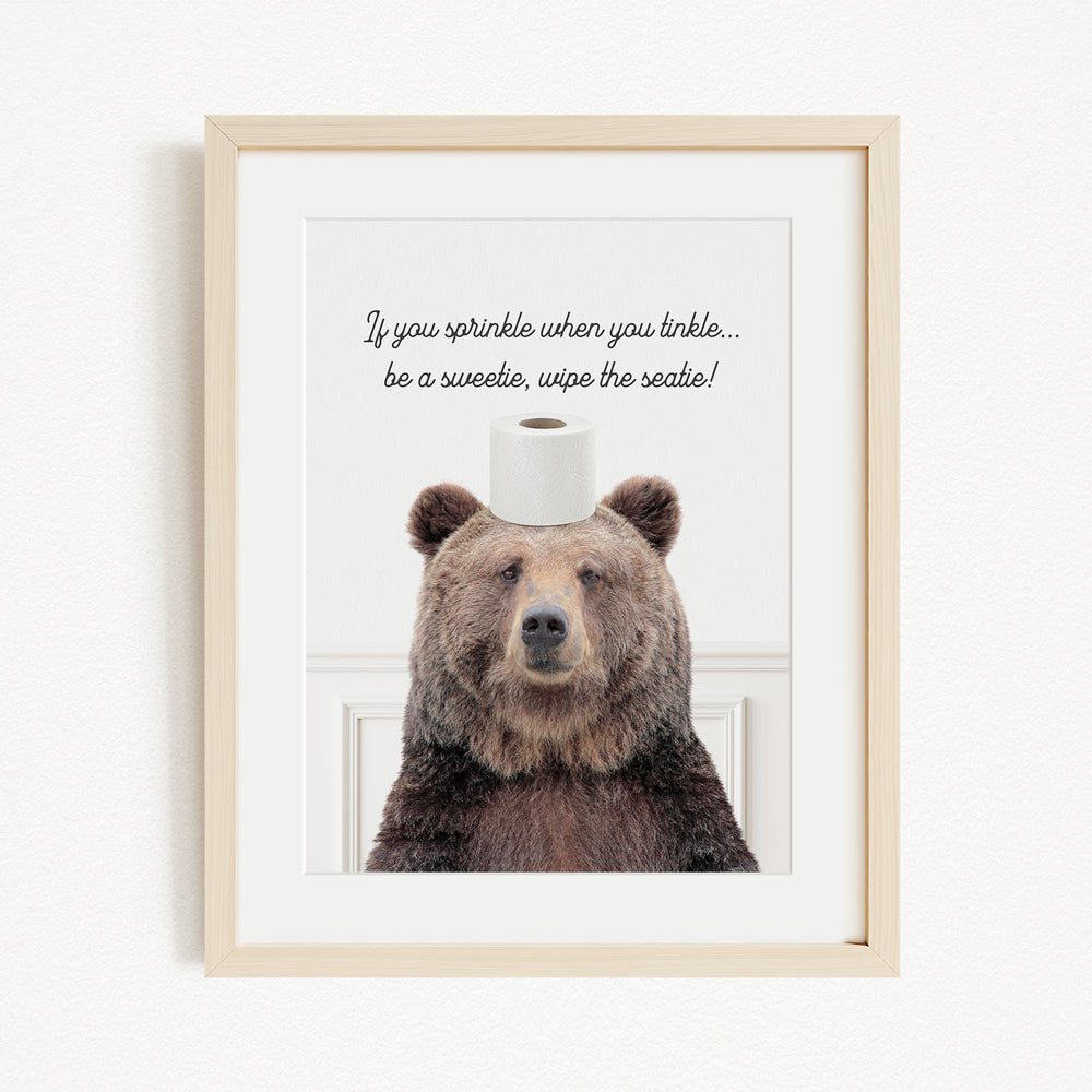 A framed image of a brown bear sitting on a roll of toilet paper, with a humorous caption below the image.