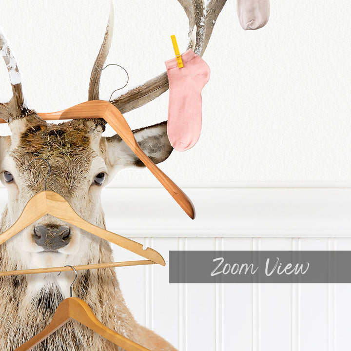 A deer head is mounted on a wall, with a pile of clothes hanging from its antlers.