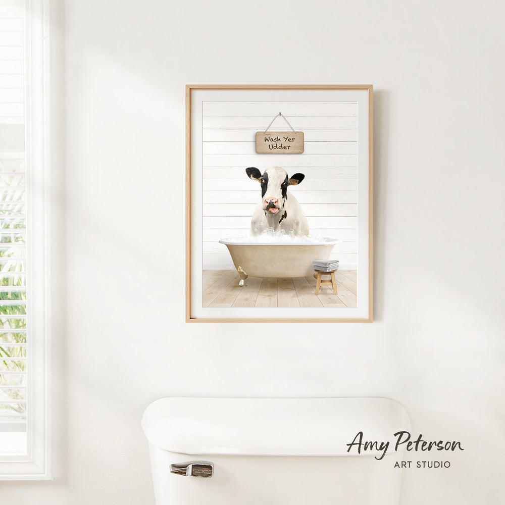A framed image of a cow sitting in a bathtub, with a sign above it that says "Wash Your Udders".