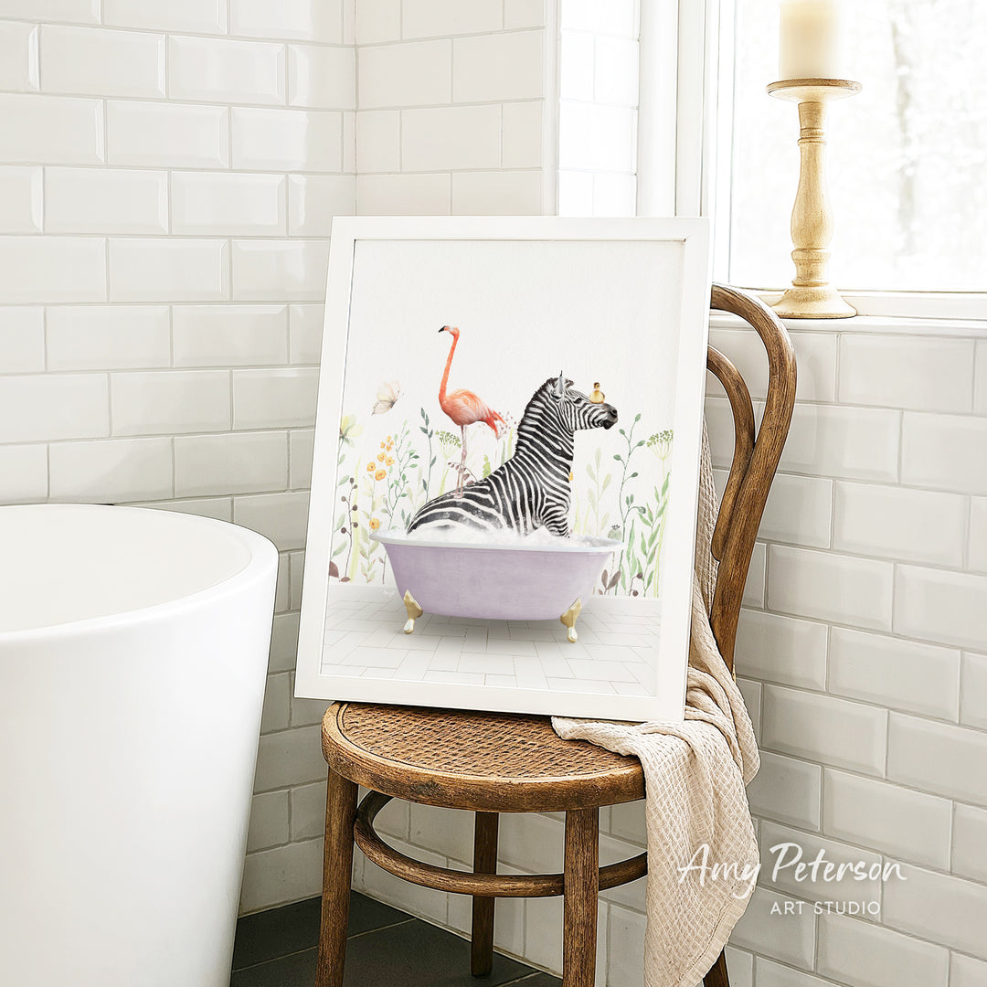 A framed illustration of a zebra sitting in a bathtub, with a pink flamingo perched on its back, is displayed on a wooden chair in a bathroom setting.