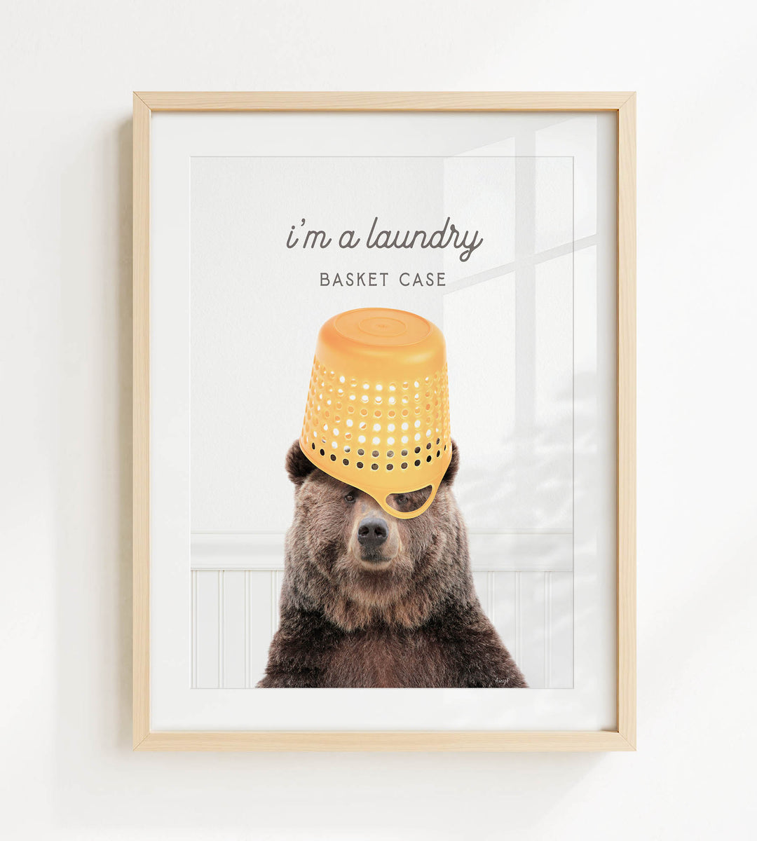 A framed image of a bear wearing a yellow plastic basket on its head, with the text "I'm a laundry basket case" above it.
