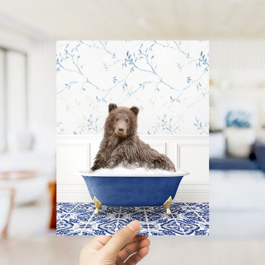 A brown bear sitting in a blue bathtub filled with bubbles, with a floral patterned wall behind it.