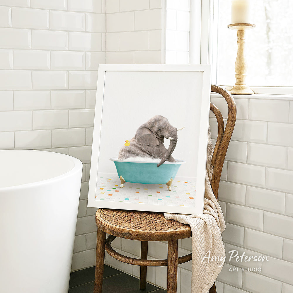 A framed image of a gray elephant sitting in a blue bathtub, surrounded by colorful tiles, is displayed on a wooden chair in a bathroom setting.