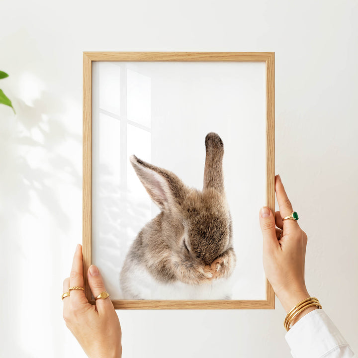 A person's hands are holding a wooden frame with a picture of a sleeping rabbit inside it.