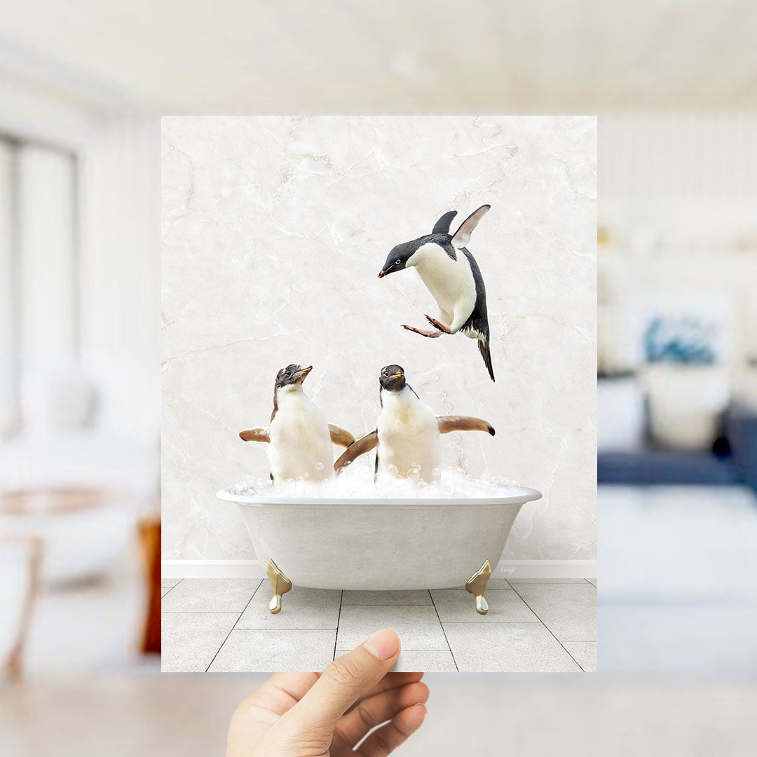 A hand holds up a framed image depicting two penguins sitting in a bathtub, with one penguin flying towards the other.