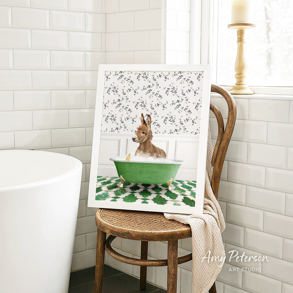 A framed image of a dog sitting in a green bathtub, surrounded by a floral pattern, is displayed on a wooden chair in a bathroom setting.