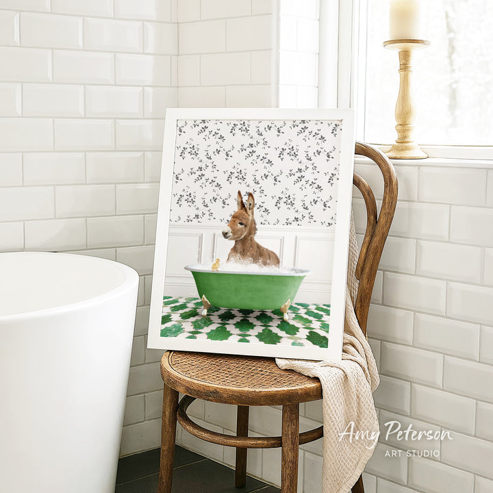A framed image of a dog sitting in a green bathtub, surrounded by a floral pattern, is displayed on a wooden chair in a bathroom setting.