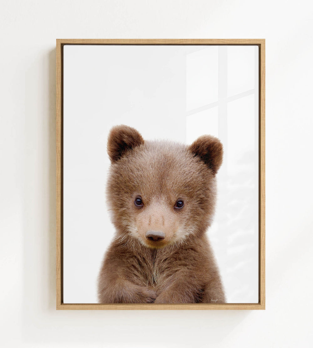 A cute brown bear cub with large eyes and a curious expression is the focus of the framed image.