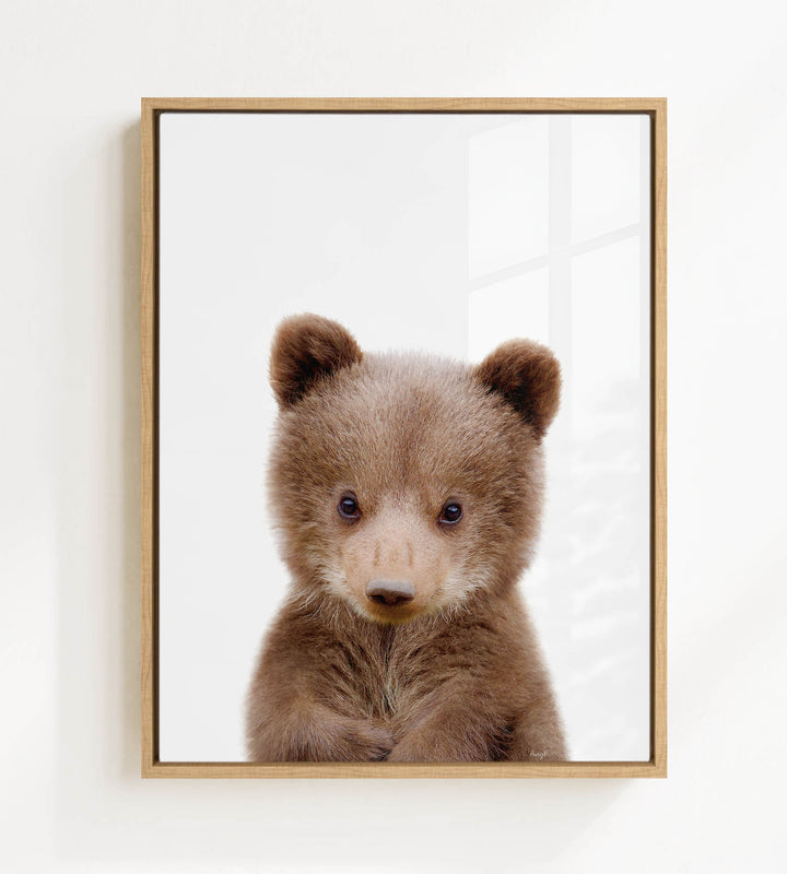 A cute brown bear cub with large eyes and a curious expression is the focus of the framed image.