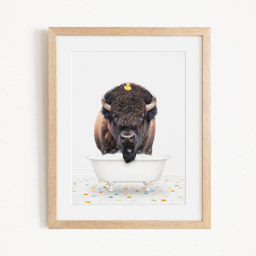 A buffalo with a yellow rubber duck perched on its head is sitting in a white bathtub, surrounded by colorful tiles on the floor.