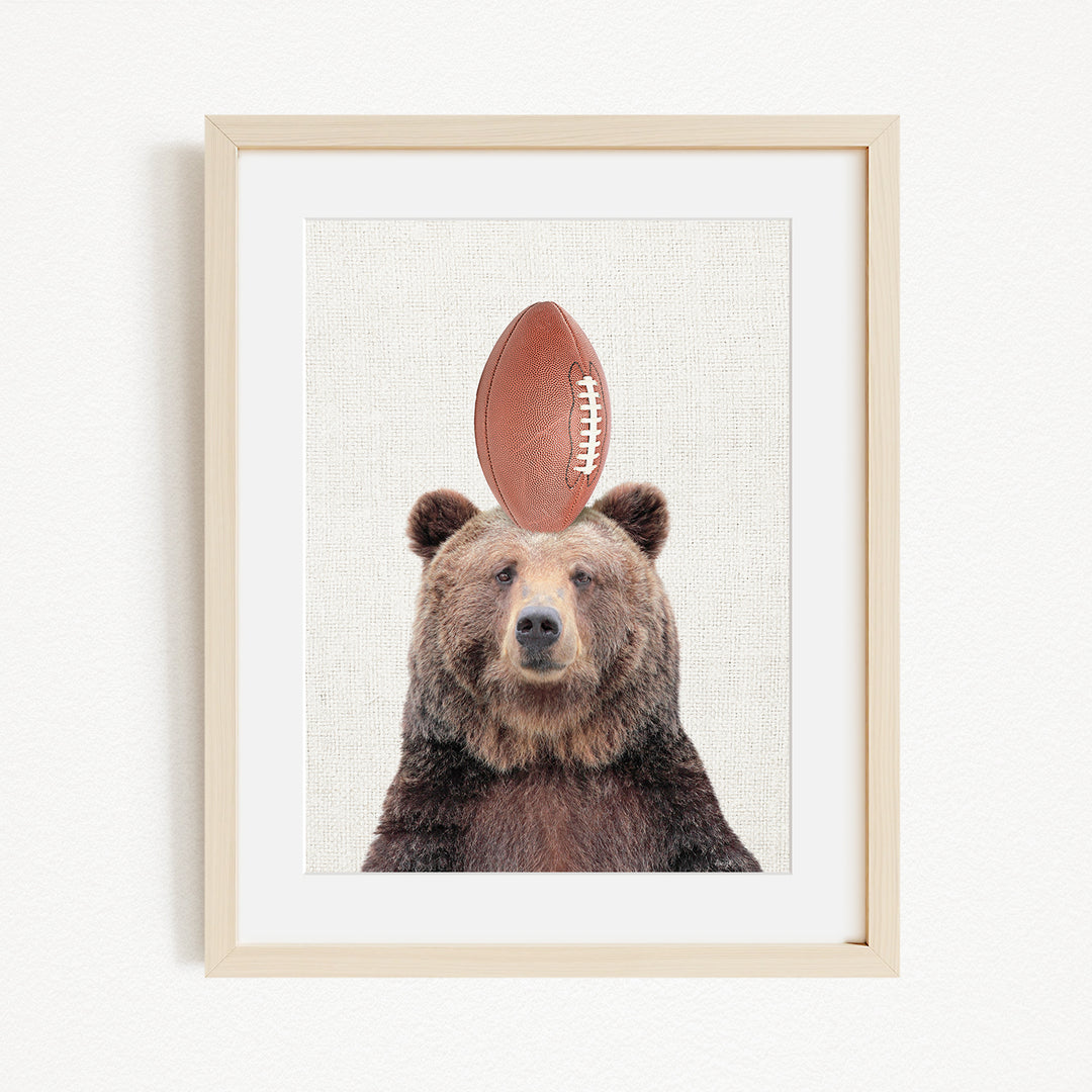 A framed image of a brown bear with a football on its head.