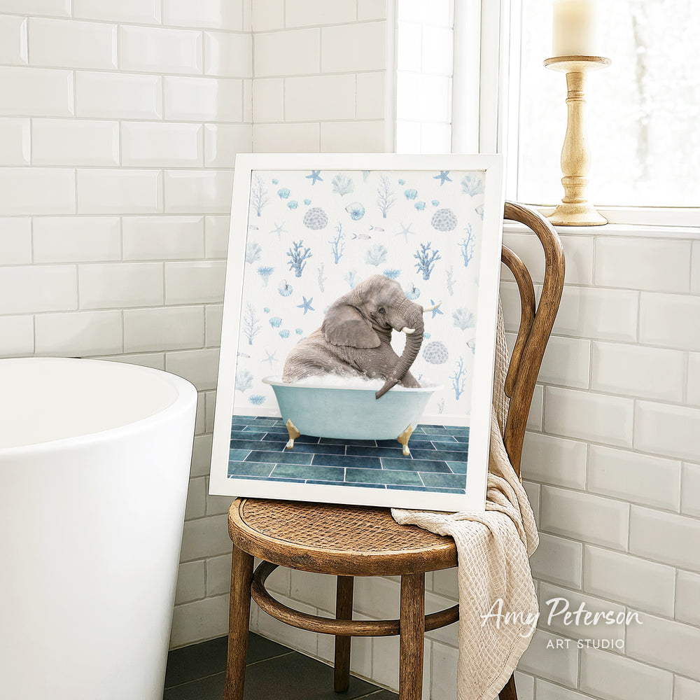 A framed image of a gray elephant sitting in a blue bathtub, surrounded by blue and white floral patterns, is displayed on a wooden chair in a bathroom setting.