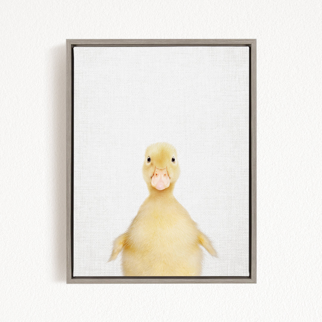 A cute yellow duck with a pink beak is looking directly at the camera in a framed picture.