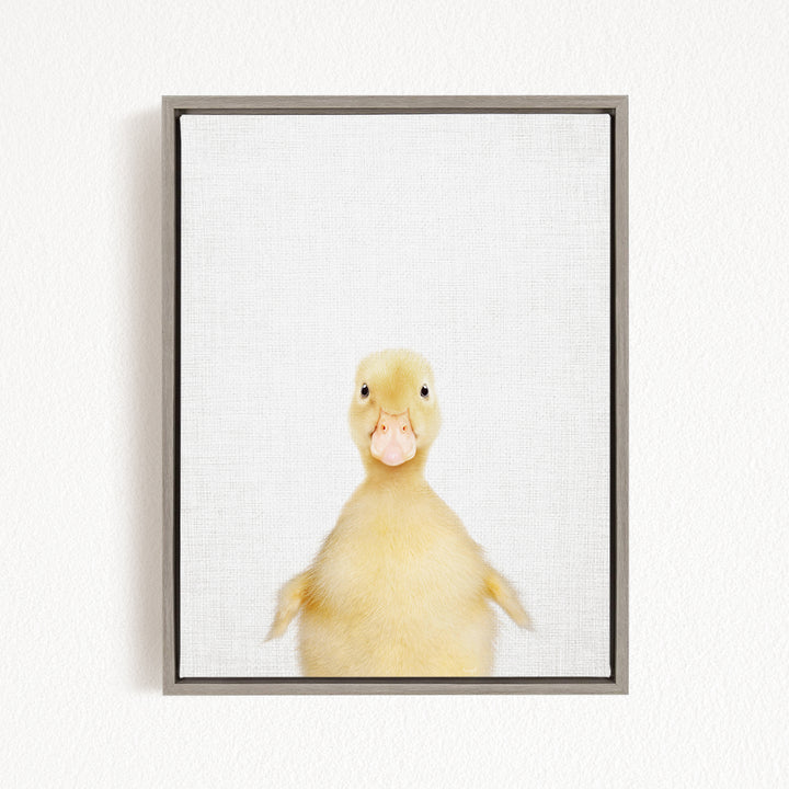 A cute yellow duck with a pink beak is looking directly at the camera in a framed picture.