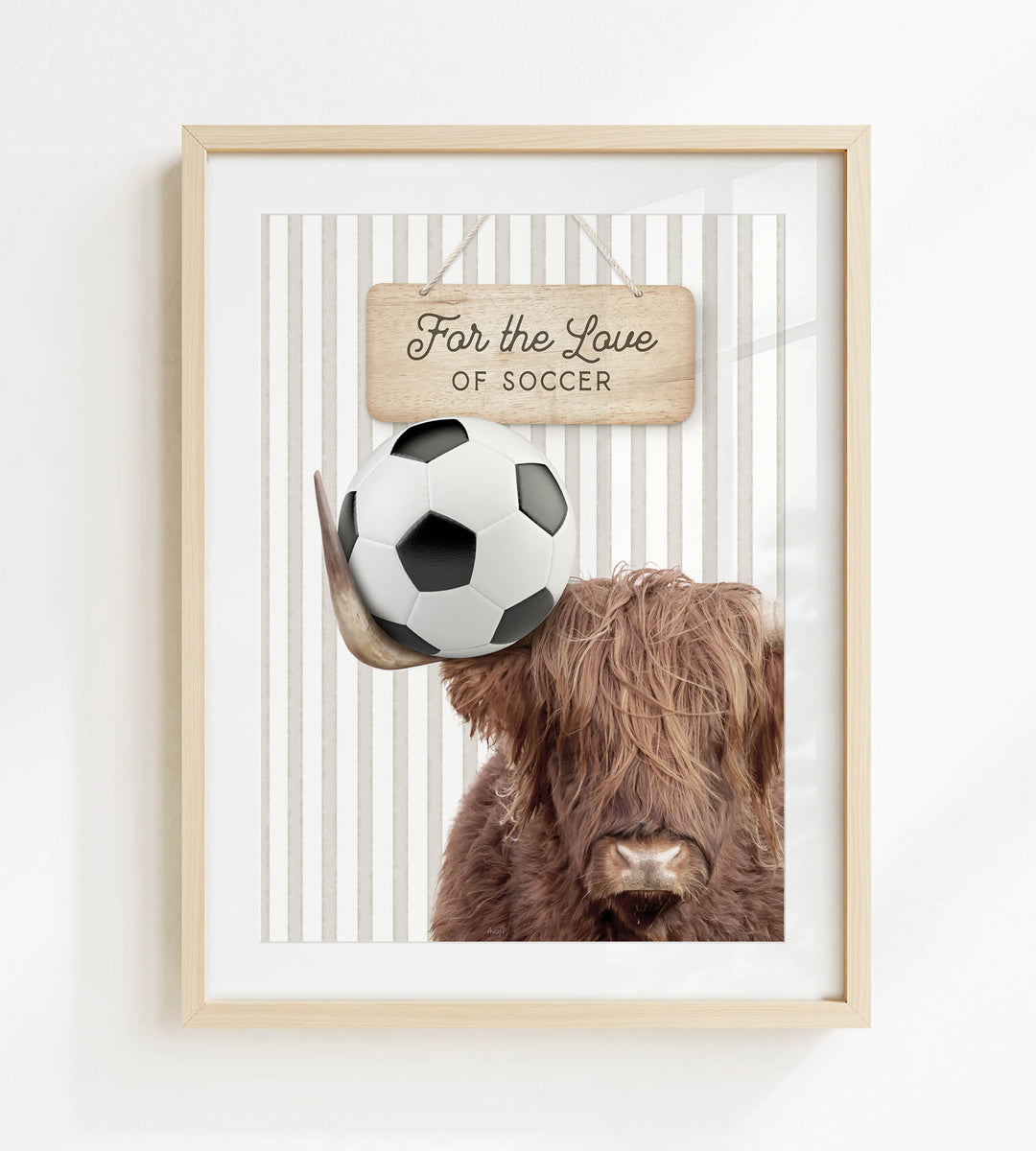 A framed image of a Highland cow holding a soccer ball, with a wooden sign above it that says "For the Love of Soccer".