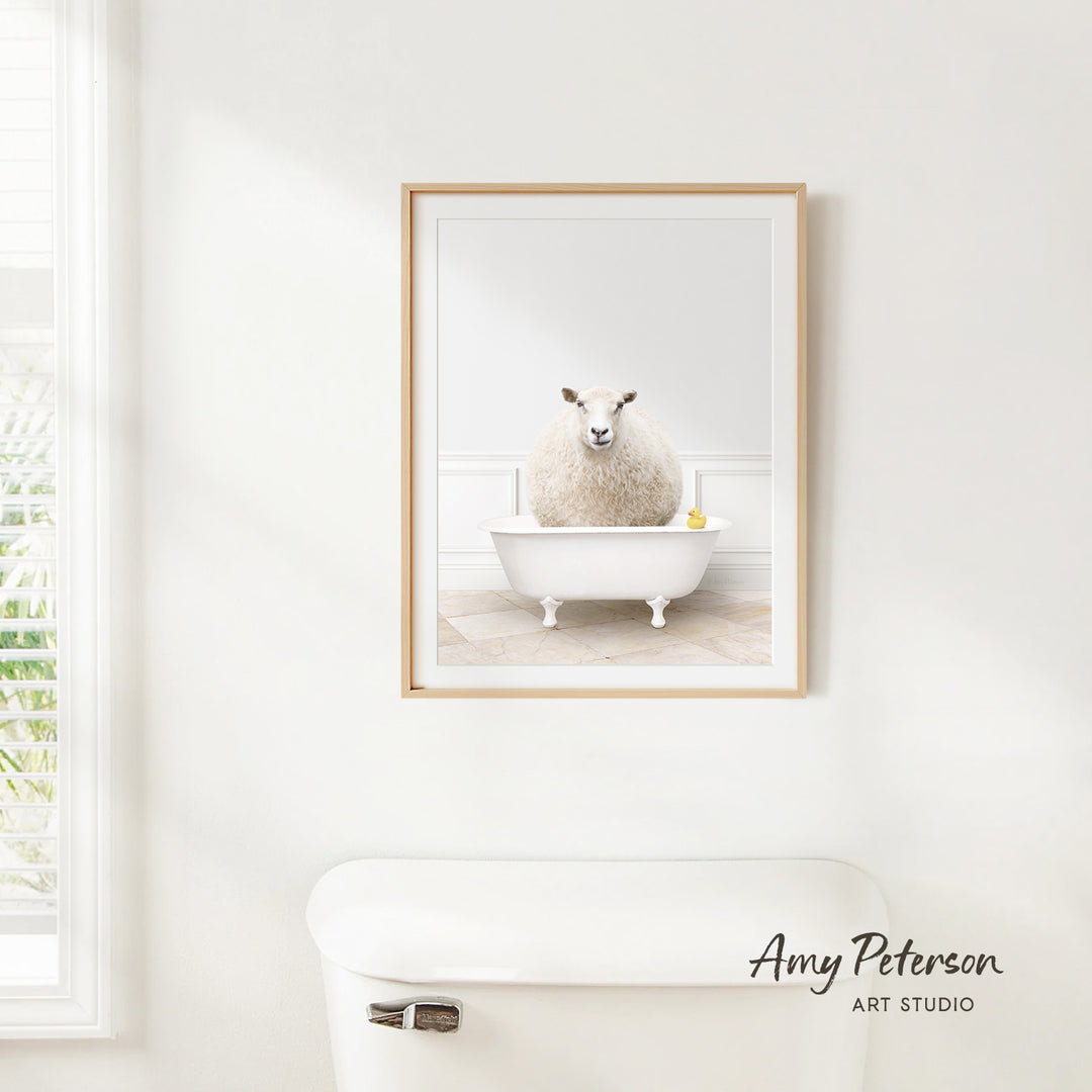 A framed image of a fluffy white sheep sitting in a white bathtub, with a yellow rubber duck floating in the water.