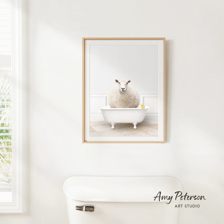 A framed image of a fluffy white sheep sitting in a white bathtub, with a yellow rubber duck floating in the water.