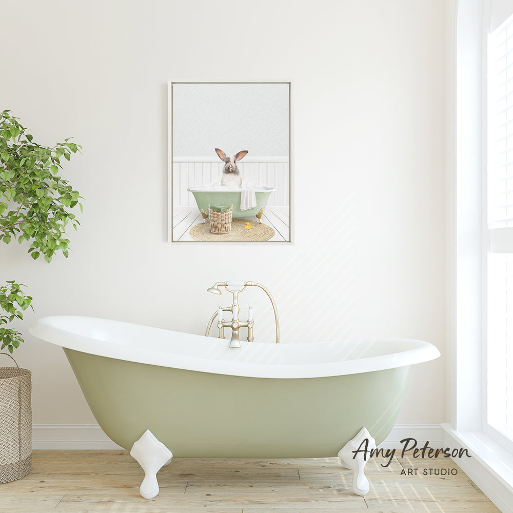 A green clawfoot bathtub sits in a bright, white bathroom, with a framed image of a rabbit sitting in the tub above it.