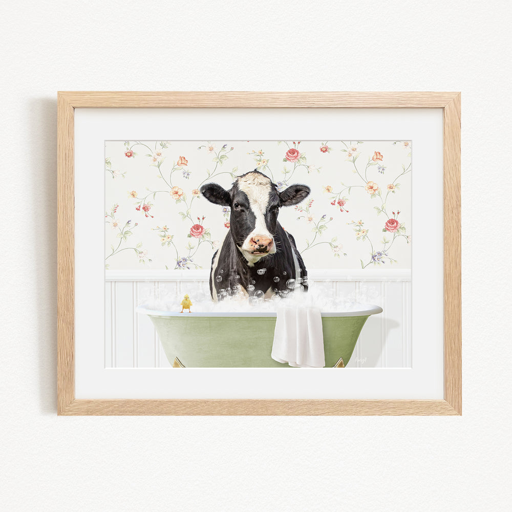 A black and white cow is sitting in a green bathtub filled with bubbles, surrounded by a floral patterned wall.