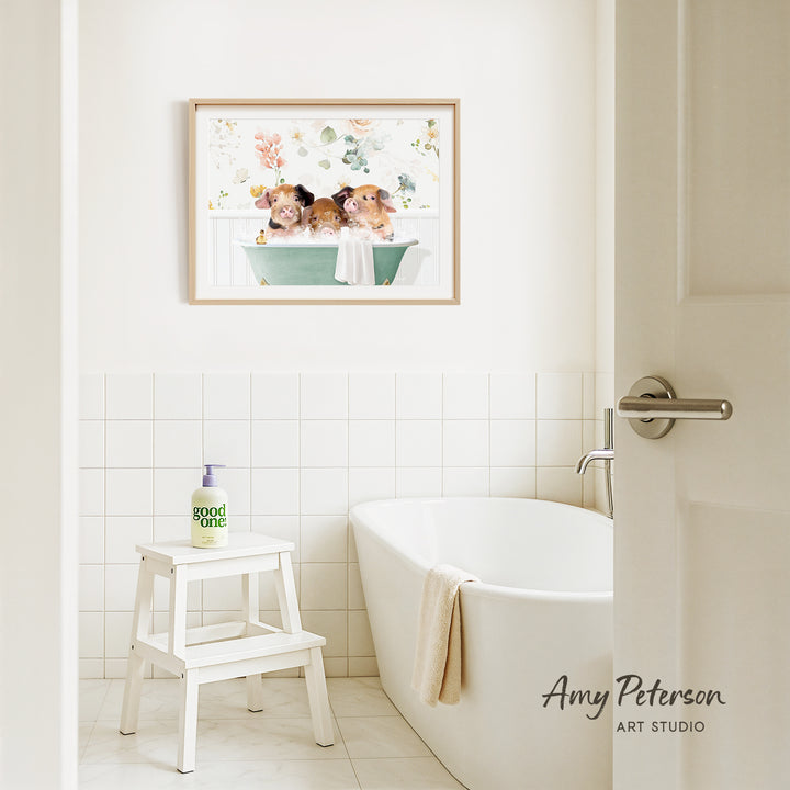 A framed painting of three guinea pigs sitting in a bathtub is hanging on the wall above a white bathtub in a bathroom.