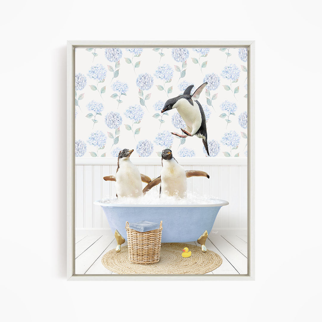 A framed image depicting two penguins sitting in a bathtub filled with water, surrounded by a blue floral patterned wall and a basket of rubber ducks.