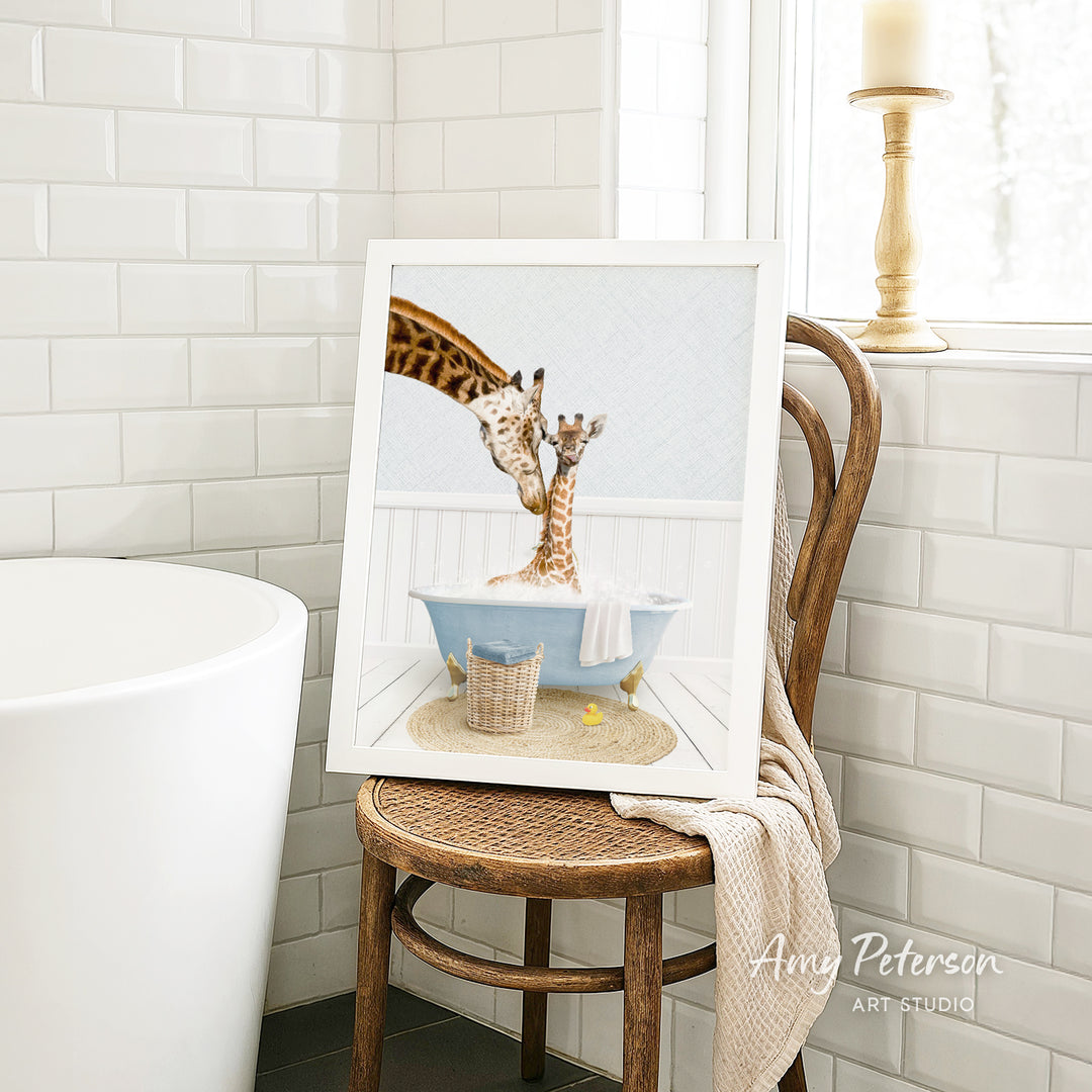 A framed image of two giraffes sitting in a bathtub, with one giraffe appearing to be bathing the other giraffe. The image is displayed on a wooden chair in a bathroom setting.