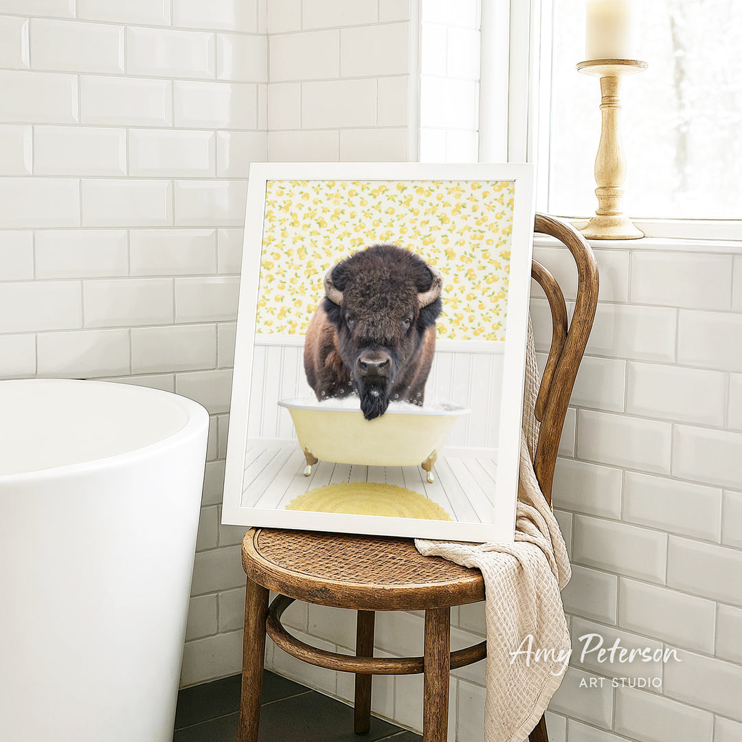A framed image of a buffalo sitting in a bathtub, with a yellow floral pattern on the wall behind it.