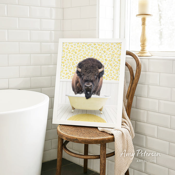 A framed image of a buffalo sitting in a bathtub, with a yellow floral pattern on the wall behind it.