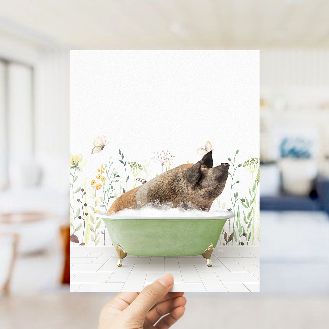 A hand holds up a framed image of a pig sitting in a green bathtub, surrounded by a floral pattern.