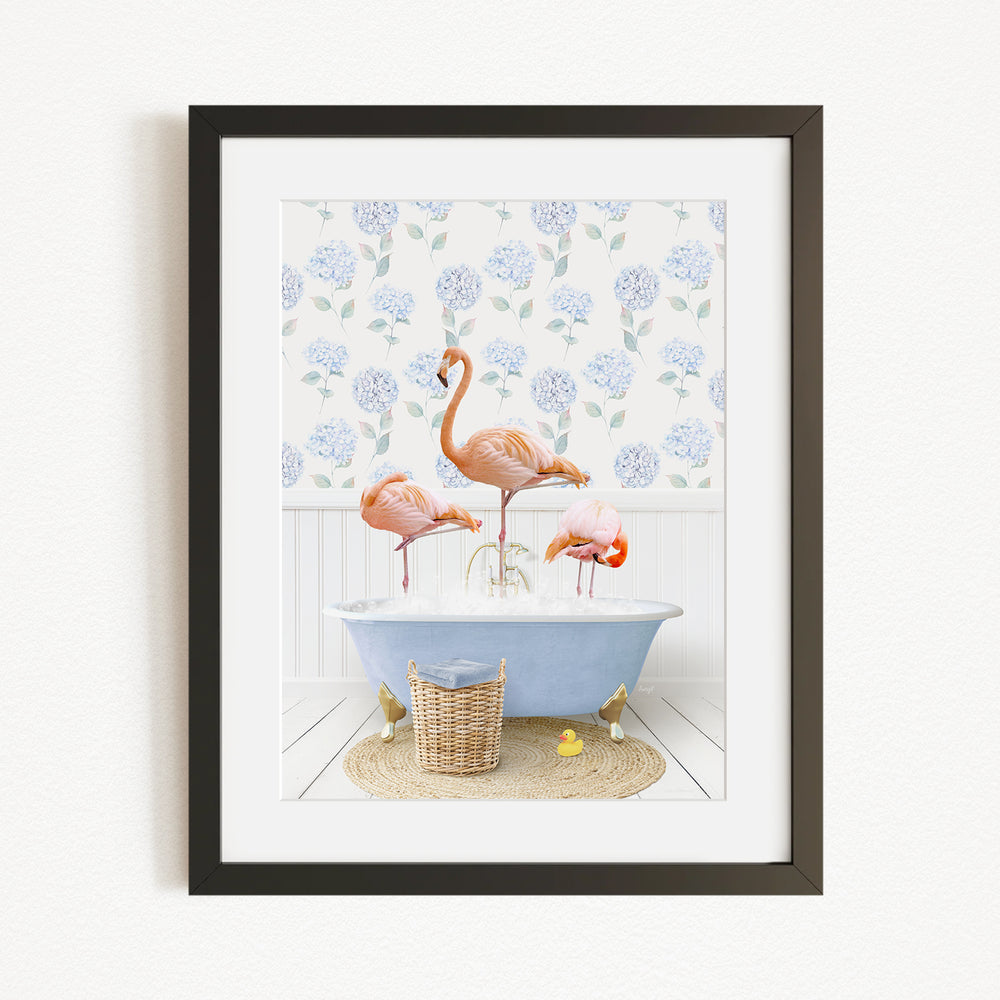 A framed image depicting three flamingos standing in a bathtub filled with water, surrounded by a blue floral pattern on the wall behind them.