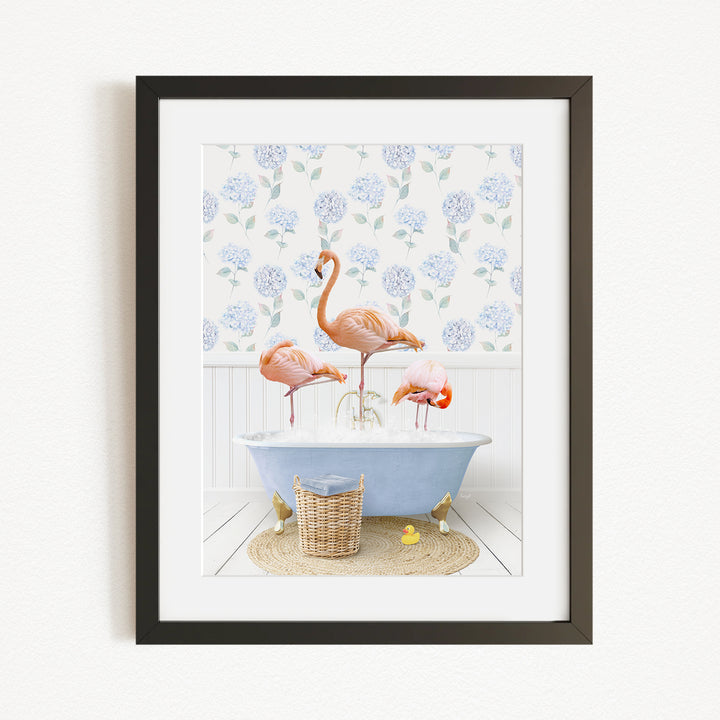 A framed image depicting three flamingos standing in a bathtub filled with water, surrounded by a blue floral pattern on the wall behind them.