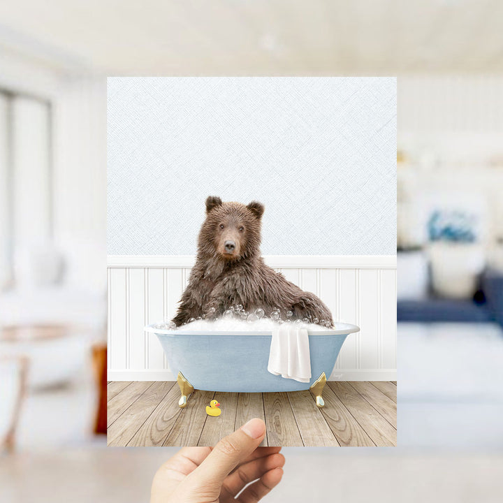 A brown bear sitting in a blue bathtub filled with bubbles, surrounded by a white bathtub, a yellow rubber duck, and a white towel.