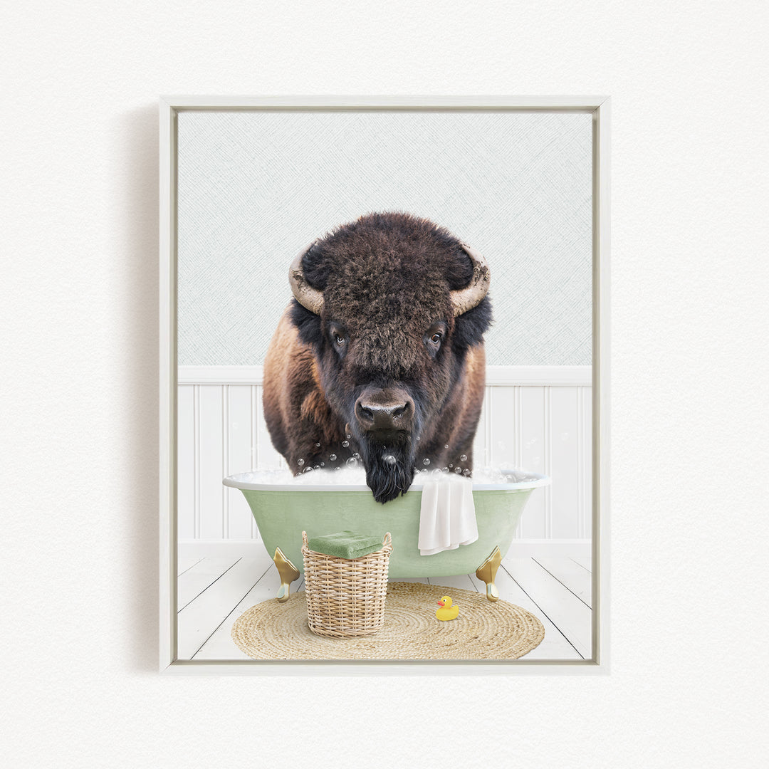 A buffalo is sitting in a green bathtub, surrounded by a basket, a yellow rubber duck, and a towel.