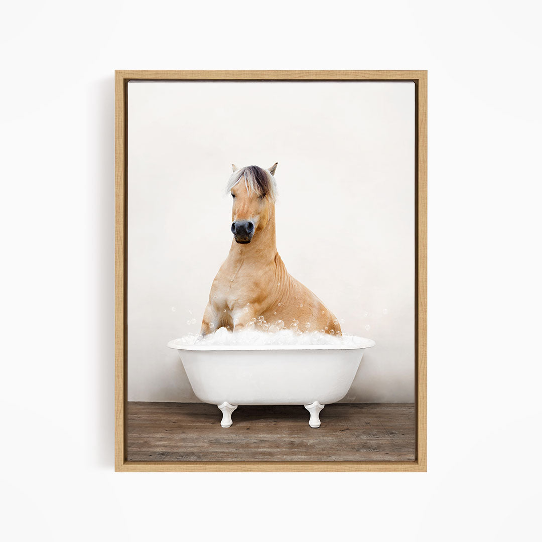 A brown horse sitting in a white bathtub filled with bubbles, with a wooden floor beneath it.