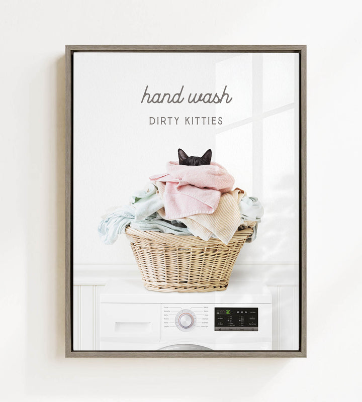 A framed image depicting a cat sitting in a basket filled with laundry, with the text "hand wash dirty kitties" above the basket.