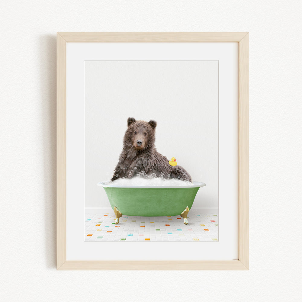 A brown bear sitting in a green bathtub filled with bubbles, with a yellow rubber duck floating on the water.