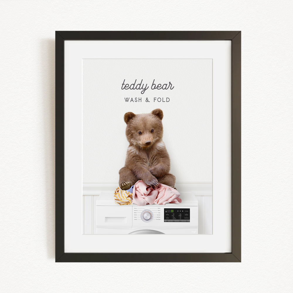 A teddy bear sitting on a washing machine, with the text "teddy bear" and "WASH & FOLD" written above it.