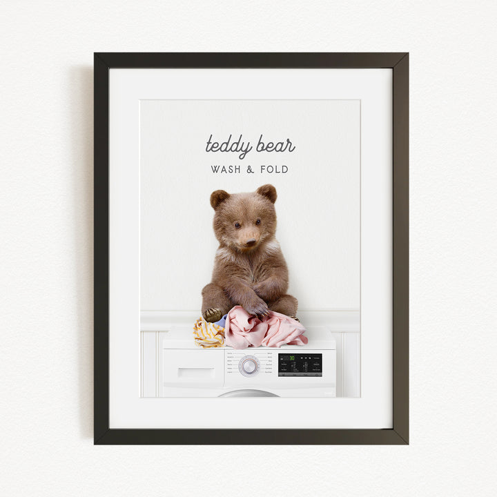 A teddy bear sitting on a washing machine, with the text "teddy bear" and "WASH & FOLD" written above it.